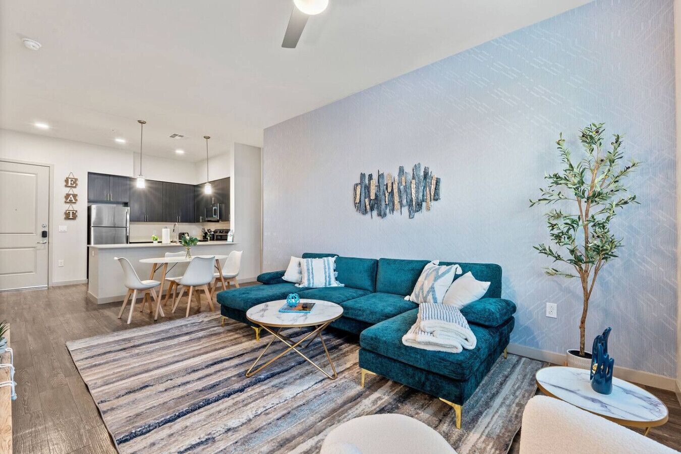 Ein modernes Wohnzimmer mit einem türkisfarbenen Sofa, einem Couchtisch und einem Essbereich mit Stühlen.