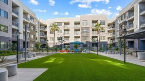 Um moderno conjunto de apartamentos com várias varandas, um pátio central com gramado e área de estar ao ar livre.