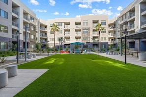 Ein moderner Wohnkomplex mit mehreren Balkonen, einem Innenhof mit Rasen und Gartenmöbeln.