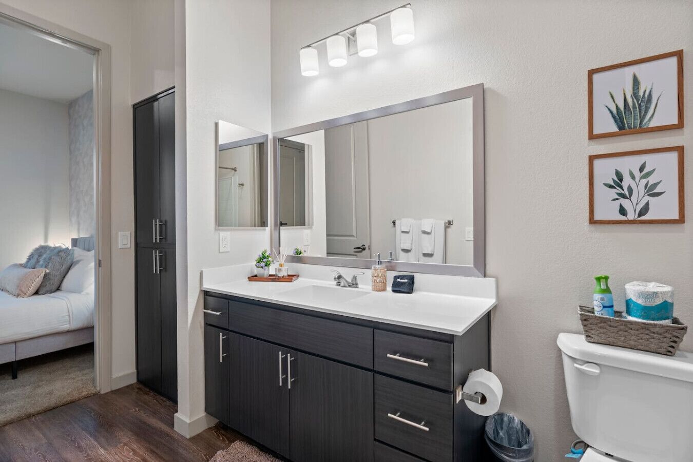 A bathroom with a large mirror, dark cabinets, a white sink, and a toilet.