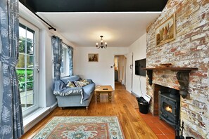 A living room with a sofa, a fireplace, and a view of the outdoors. - Welcoming Cottage in Kent Village (Tonbridge)