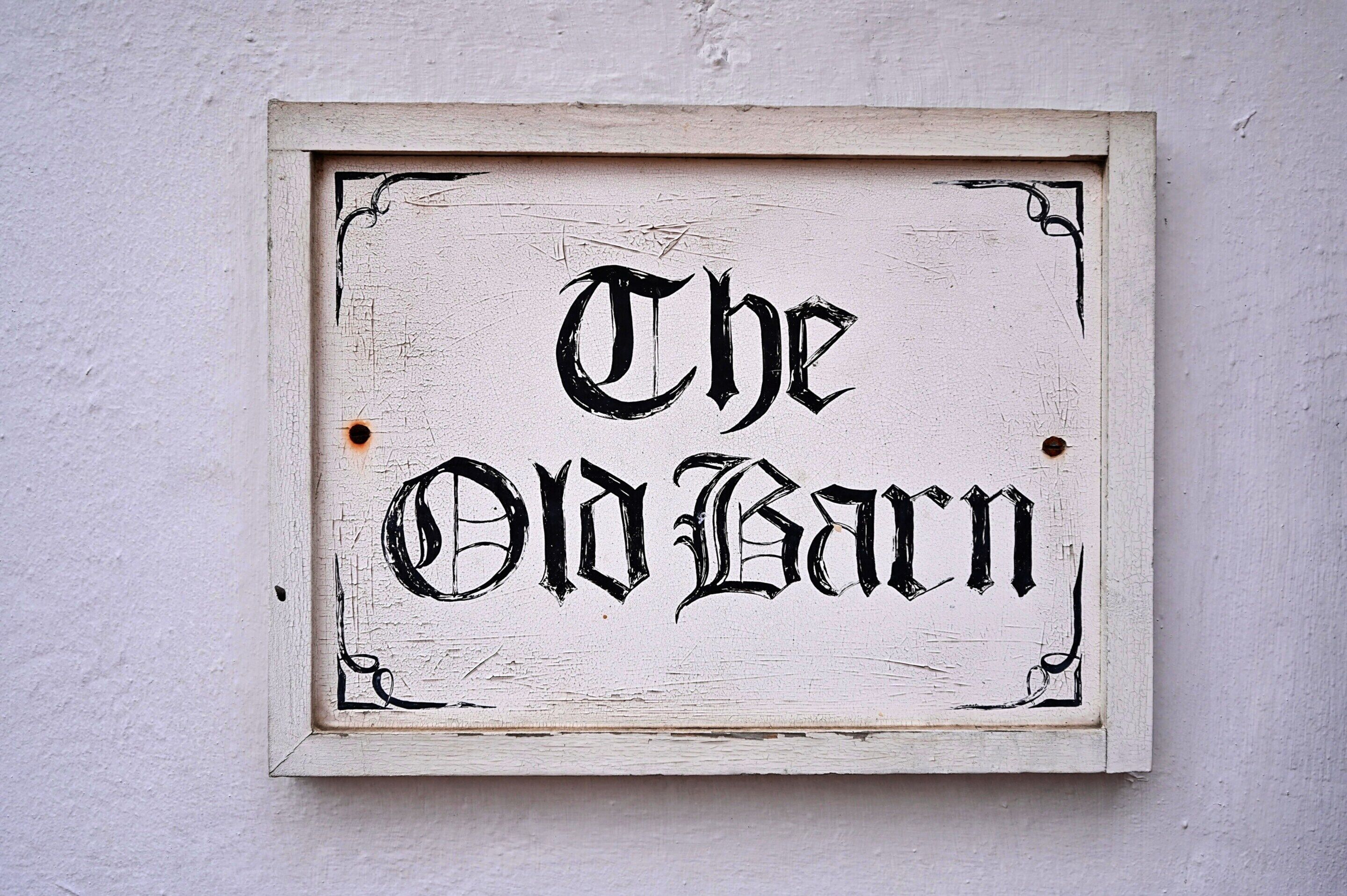 Un letrero blanco y desgastado con letras negras que dicen 'The Old Barn'.