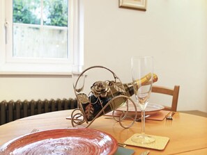 A table with a bottle of champagne, a glass, a red plate, and a wooden chair. - Welcoming Cottage in Kent Village (Tonbridge)