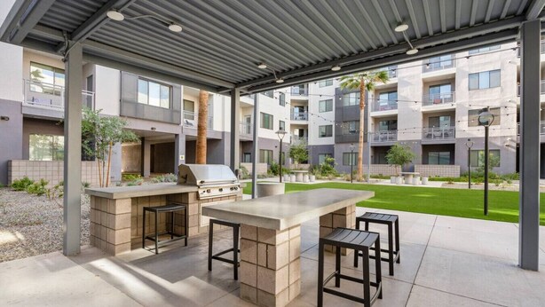 An outdoor patio area with a barbecue grill, seating, and a view of residential buildings. - Desert Oasis - Pool, Gym, Courtyard - King Bed (Tempe)