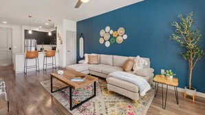 A modern living room with a sofa, coffee table, and a dining area with chairs. - Desert Oasis - Pool, Gym, Courtyard - King Bed (Tempe)