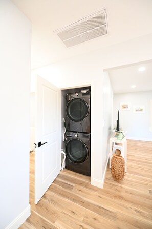 A laundry room with two stacked front-loading washers and dryers, a white door, and a small white cabinet with a woven basket. - Perfect 4-bedroom house located outside of the quaint town of Beaufort! (Beaufort)