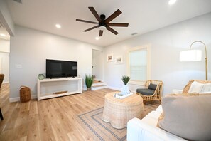 A modern living room with a flat-screen TV, a ceiling fan, a wicker coffee table, and a rattan chair. - Perfect 4-bedroom house located outside of the quaint town of Beaufort! (Beaufort)
