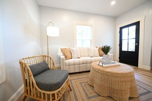 A living room with a wicker chair, a sofa, a floor lamp, and a door. - Perfect 4-bedroom house located outside of the quaint town of Beaufort! (Beaufort)