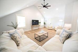 Uma sala de estar moderna com teto alto, televisão de tela plana, mesa de centro e sofá com almofadas estampadas.