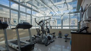 A gym with exercise equipment, large windows, and a view of buildings. - Hotel Centro Europeu (Curitiba)