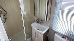 A bathroom with a glass shower enclosure, a white sink with a mirror above it, and a toilet with a window above.