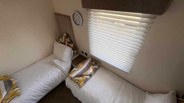 A compact room with two single beds, a clock on the wall, and a window with blinds.