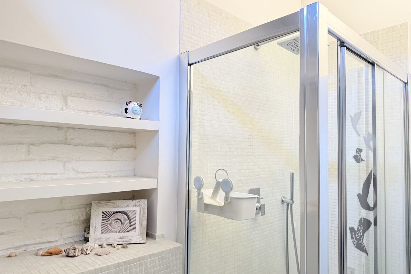 Un bagno con box doccia in vetro, pareti rivestite di piastrelle bianche e mensole con oggetti decorativi.