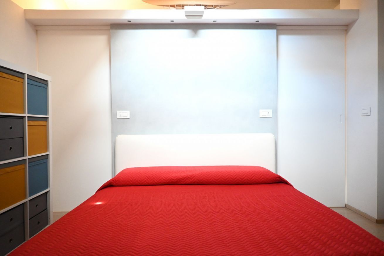 A small, compact room with a single bed, a white headboard, and a built-in wardrobe with multiple compartments.
