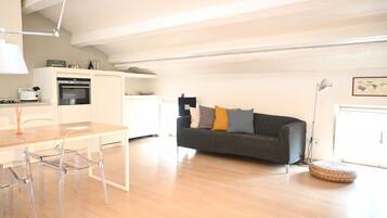 A modern kitchen with a dining area, a grey sofa with cushions, and a lamp.