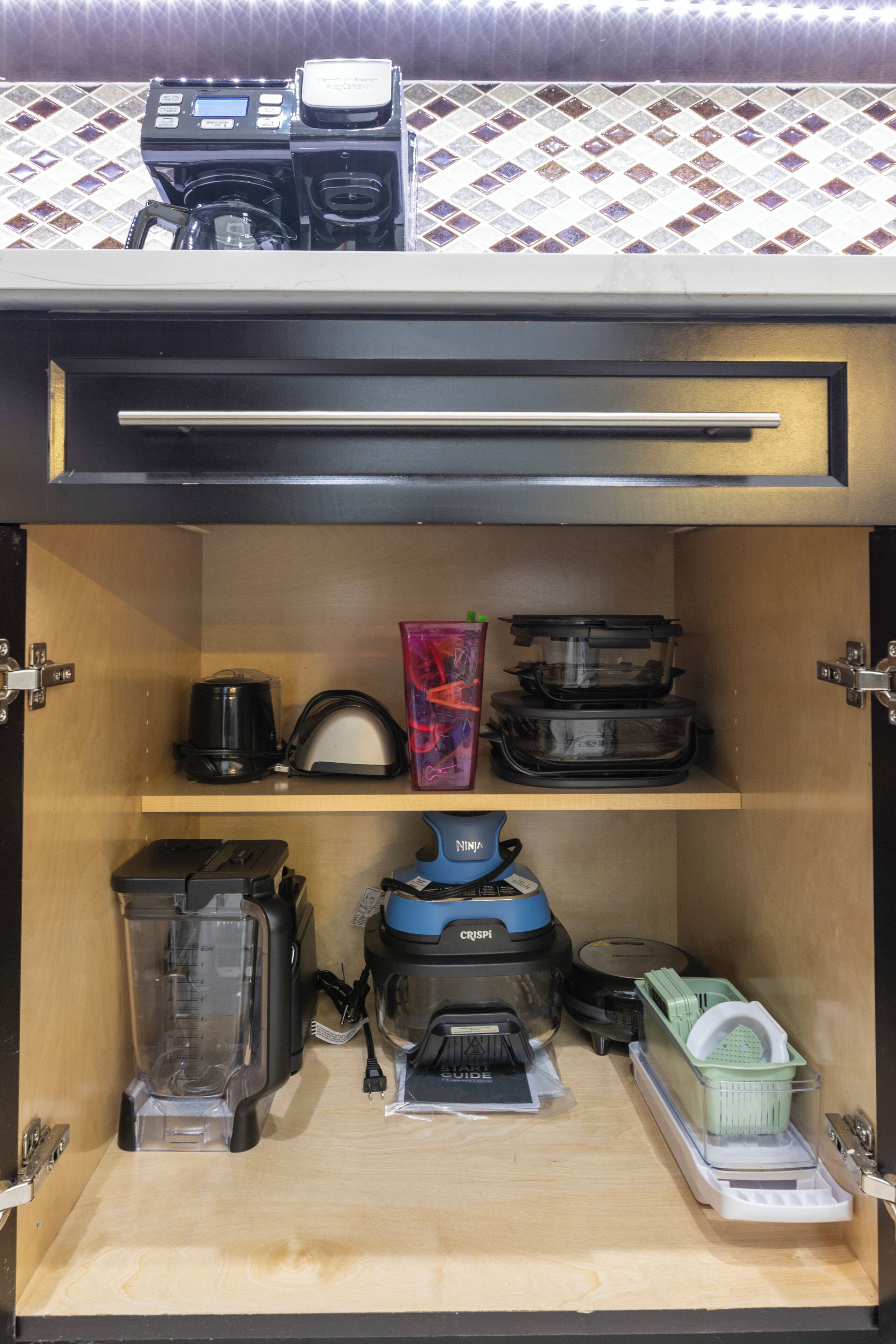 A kitchen with a coffee maker, a blender, a vacuum cleaner, and a trash bin.