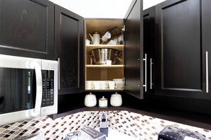 Een moderne keuken met donkere kastjes, een ingebouwde magnetron, een koffieapparaat en een betegelde achterwand.