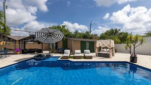 A swimming pool with lounge chairs and a covered seating area. - Luxury Villa Pool with Game Room Deerfield Beach (Pompano Beach)