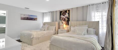 A bedroom with two beds, a nightstand, a painting, and a window with curtains.
