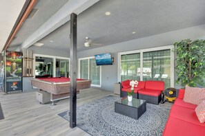 Ein modernes Wohnzimmer mit Billardtisch, rotem Sofa und einem großen Fenster.