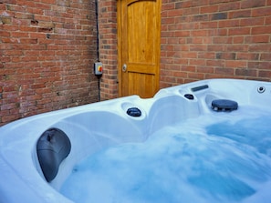 Ein Whirlpool mit Holztür und Backsteinwand im Hintergrund.