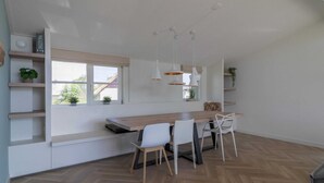 Una cocina moderna con encimera de madera, sillas blancas, iluminación colgante y vistas por la ventana.