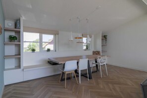 Eine moderne Küche mit Holzarbeitsplatte, weißen Stühlen, Pendelleuchten und Blick durch das Fenster.