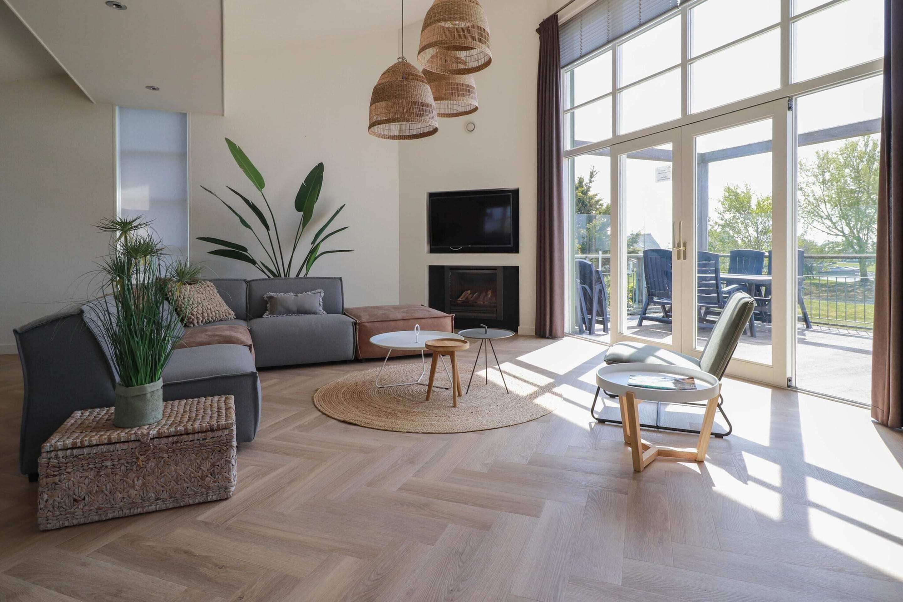 A modern living room with a sofa, coffee table, and chairs, a fireplace, and large windows.
