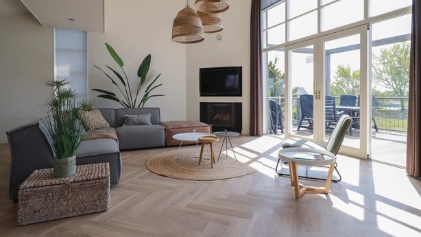 Una sala de estar moderna con un sofá, una mesa de centro, sillas, una chimenea y ventanas amplias.