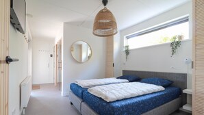 Un dormitorio con cama, un espejo redondo, una lámpara colgante y una ventana con plantas.