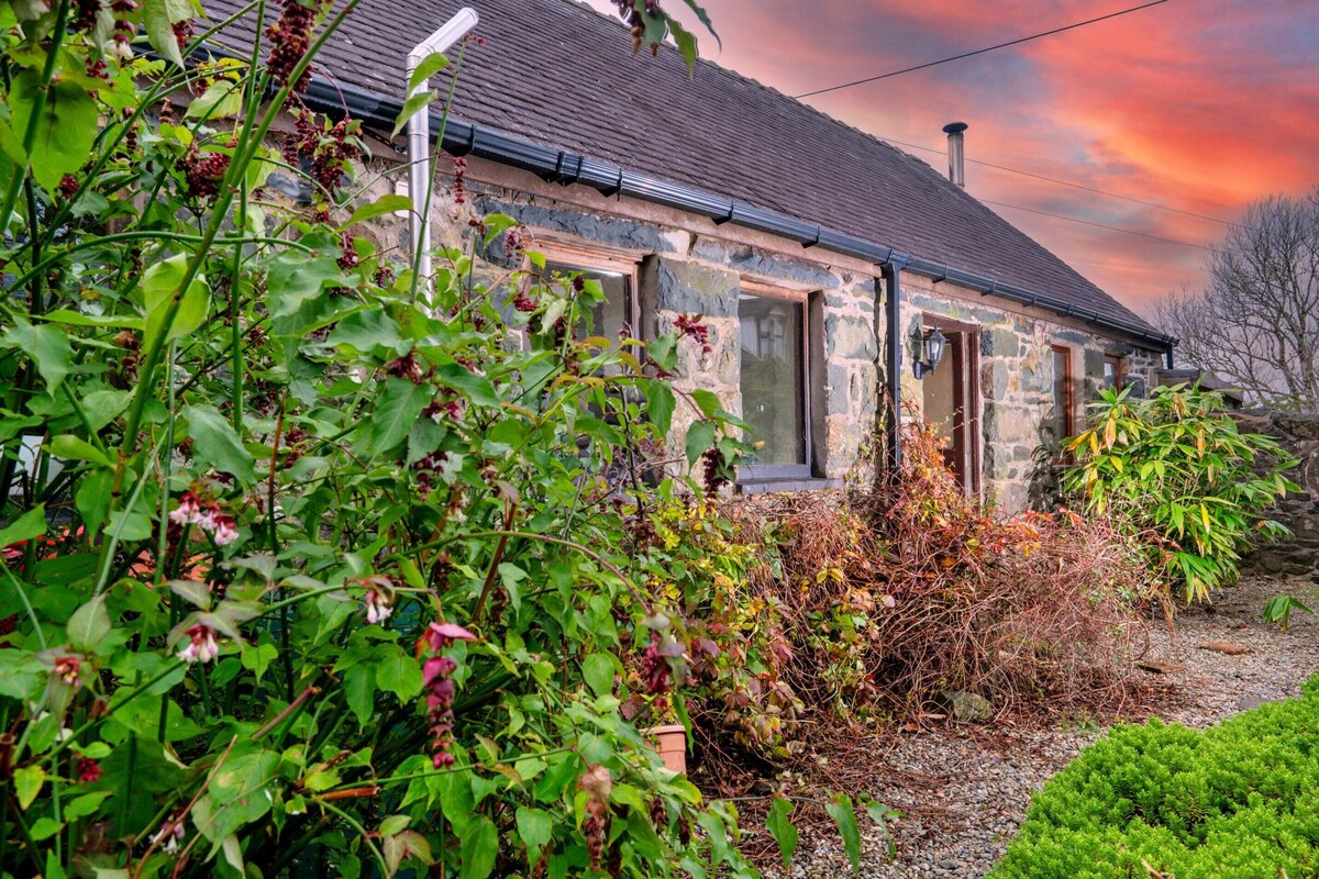 Une maison en pierre avec un toit en pente, une fenêtre visible et une porte.