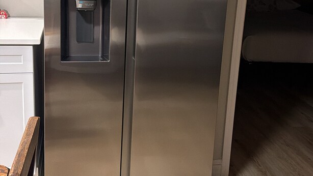 A stainless steel refrigerator with a water dispenser, located in a kitchen with wooden flooring and white cabinetry.