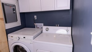 A compact laundry room with a front-loading washing machine and dryer, white cabinets above, and a wooden floor.