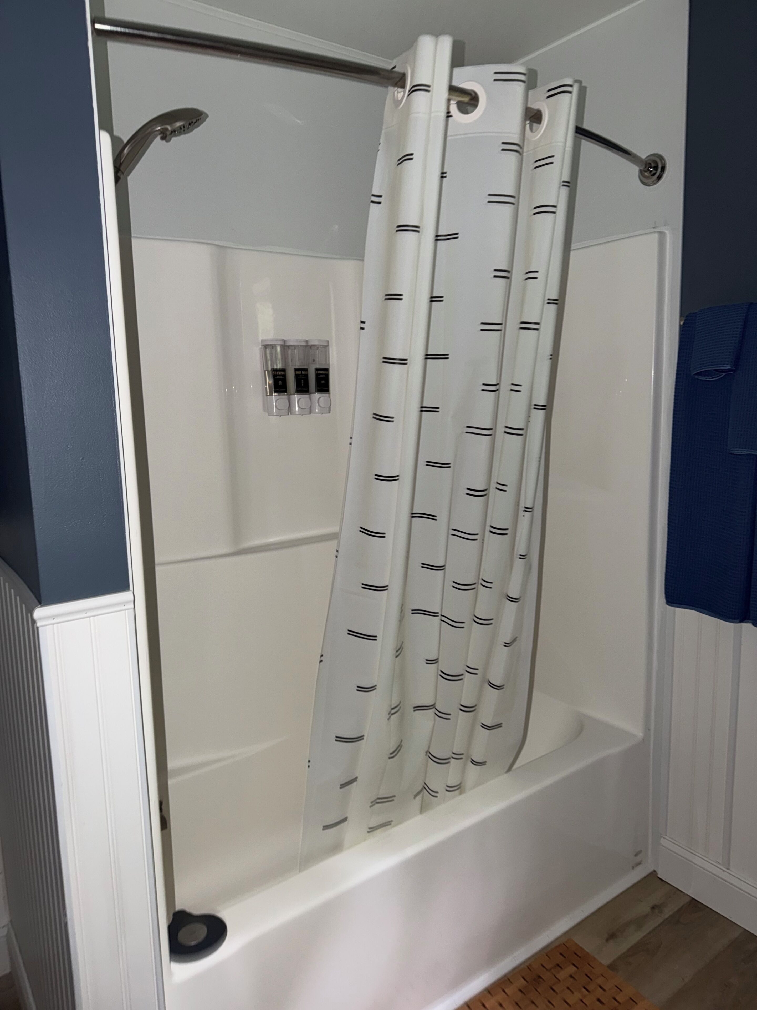 A shower with a white curtain featuring a pattern of lines and a handheld showerhead.