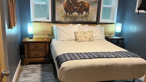 A bedroom with a bed, nightstands, a painting, and a ceiling fan.