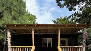 A wooden cabin with a porch, a set of stairs, and a window.