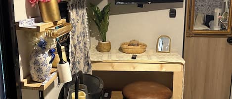 A compact kitchenette with a TV, a small stool, a marble table, and a wooden counter.