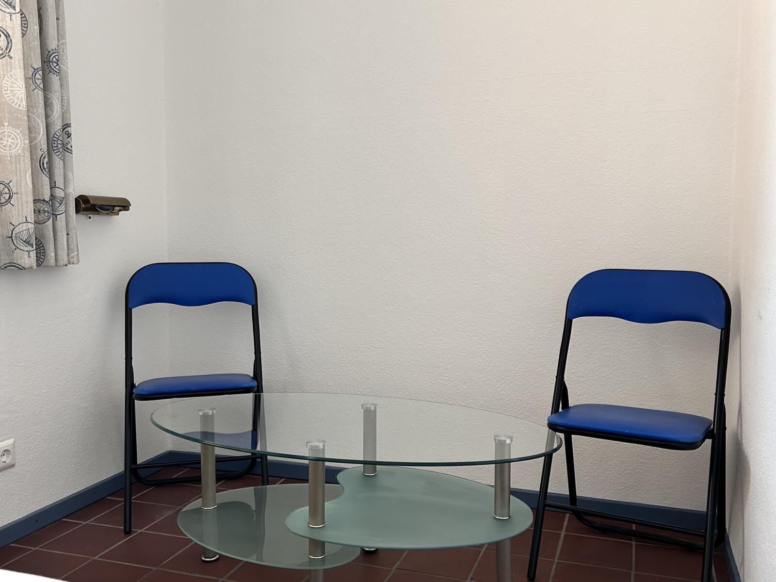 Un petit espace clos, avec une table en verre et deux chaises bleues.