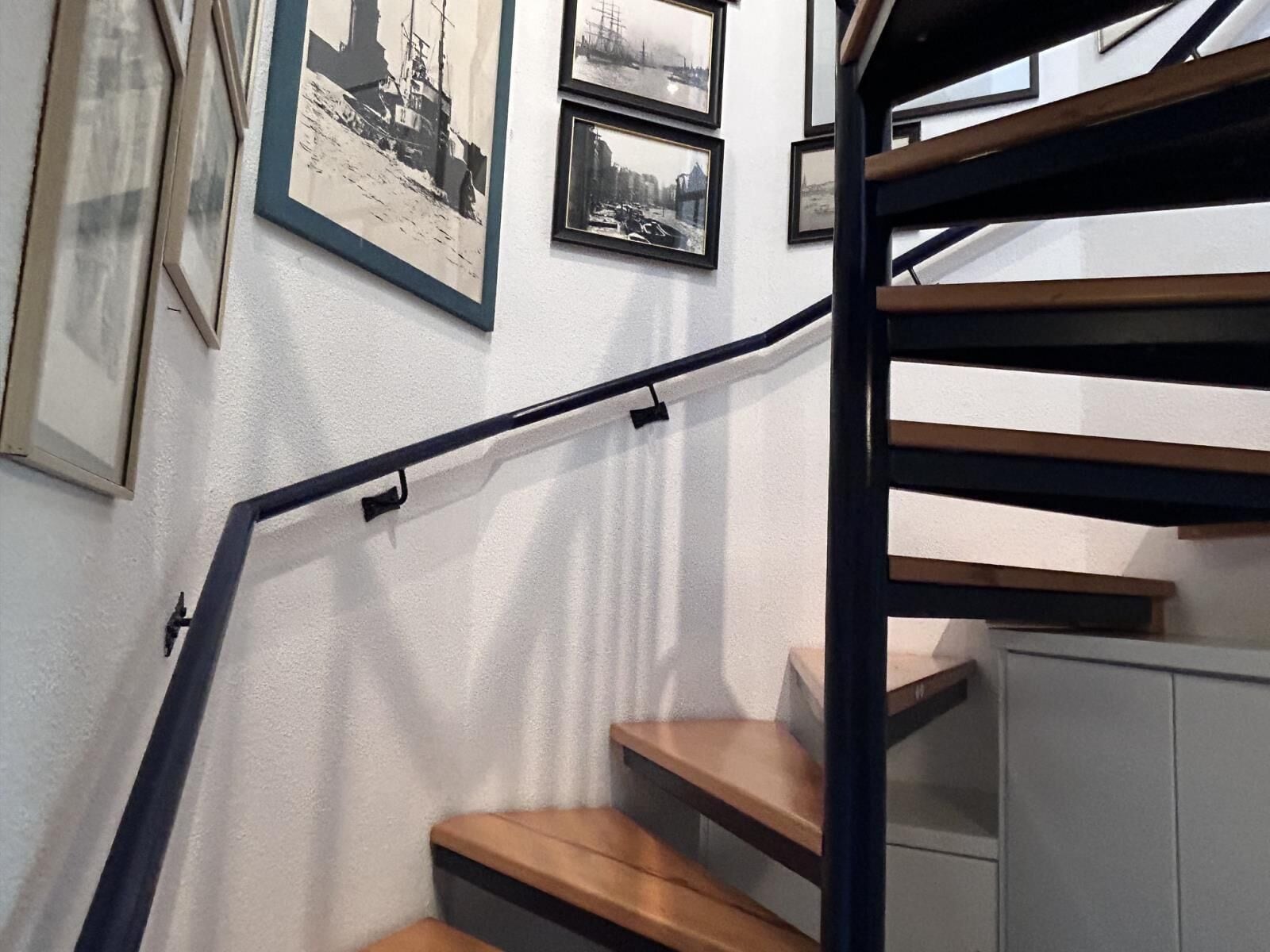 A staircase with wooden steps and a black handrail, leading to a landing with a white cabinet.