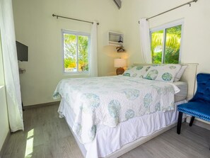 Ein Schlafzimmer mit einem Bett, einem Sessel, einem Fernseher und einem Fenster mit Vorhängen.