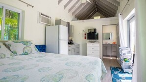 A bedroom with a bed, a kitchenette, a ceiling fan, and a window with curtains. - Turks & Caicos Retreat | 1BR Private | Experiences (Providenciales)