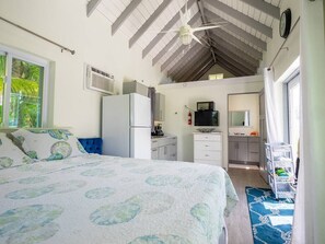 A bedroom with a bed, a kitchenette, a ceiling fan, and a window with curtains. - Turks & Caicos Retreat | 1BR Private | Experiences (Providenciales)