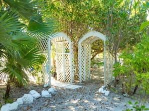 Ein Gartenweg mit weißen Gitterkonstruktionen, umgeben von Grünpflanzen und Steinen.