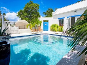 A clear swimming pool with a blue border, surrounded by a white building with blue trim and a blue door. - Turks & Caicos Retreat | 1BR Private | Experiences (Providenciales)