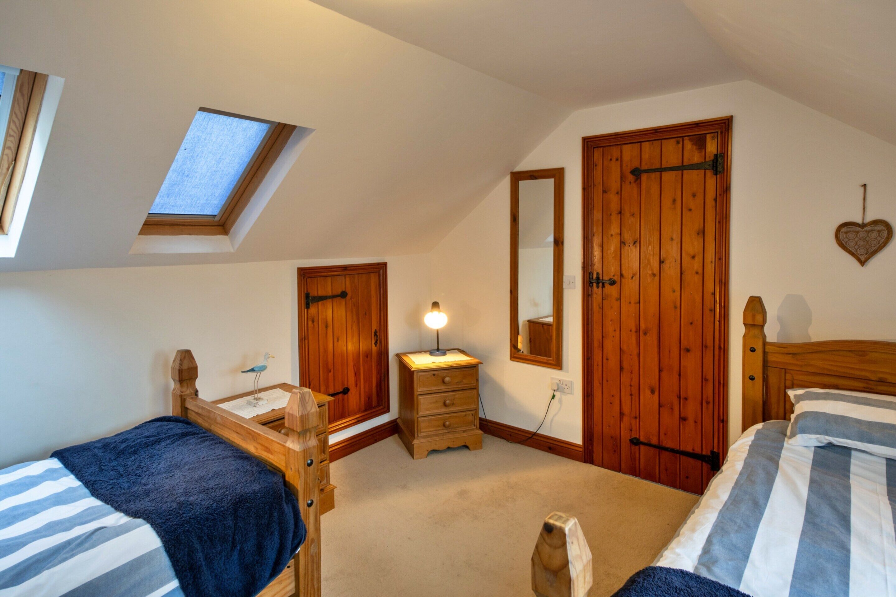 A bedroom with two beds, a skylight, a wooden wardrobe, a dresser, and a mirror.