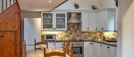 A kitchen with white cabinets, a Bosch refrigerator, a tiled backsplash, and a wooden dining table with chairs.