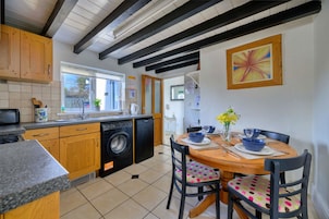 Una cocina con armarios de madera, una lavadora y una zona de comedor con una mesa para dos.
