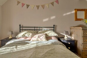 Un dormitorio con una cama, dos mesitas de noche, un aparador, un espejo y una pared decorada con guirnaldas.