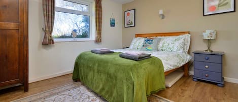 Un dormitorio con cama, mesita de noche, lámpara, ventana con cortinas y puerta.