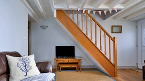 Ein Wohnzimmer mit einer Couch, einem Fernseher auf einem Holzschrank, einer Treppe mit Holzbalken und einer Tür mit Spiegel.